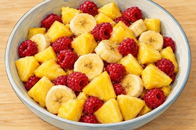 Close overhead view of pineapple pieces, banana rounds and raspberries in one low fruit bowl.